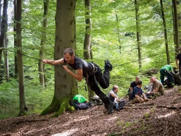 Mann überquert selbstgebaute Seilbrücke zwischen zwei Bäumen im Wald