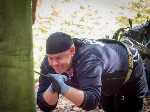 Mann zieht an einem Seil, während er sich an einem Baum abstützt