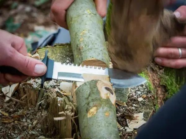 Messer bearbeitet Holzstück mit Kerbe, während ein anderer Stock darauf schlägt