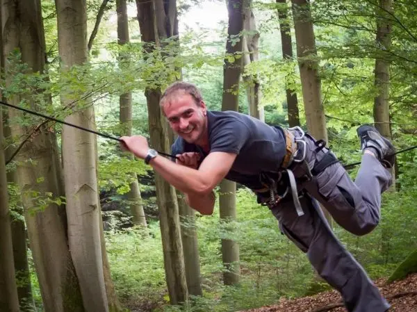 Person schwingt an einem Seil zwischen Bäumen