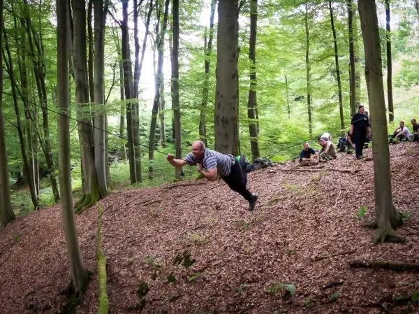 Person schwingt an Seil zwischen Bäumen im Wald beim Survival Training
