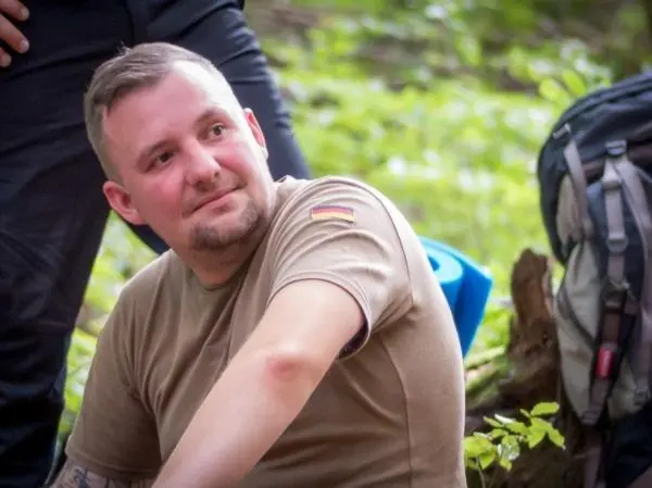 Person sitzt im Wald neben einem Rucksack und schaut nachdenklich