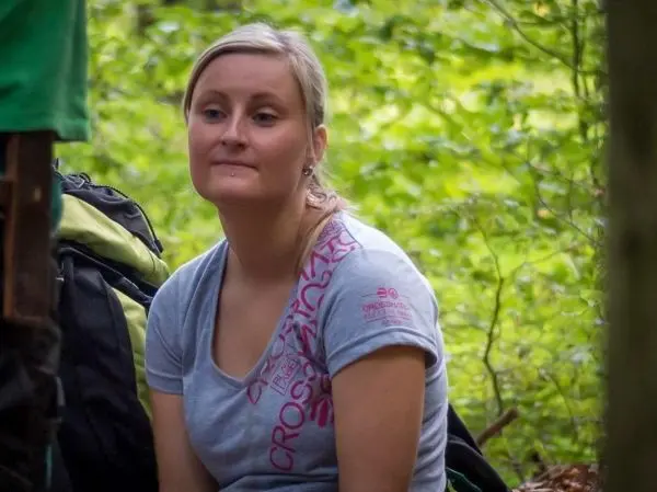Person sitzt neben Rucksack im Wald