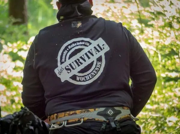 Person trägt einen schwarzen Hoodie mit Aufdruck im Wald