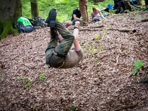 Person überquert selbstgebaute Seilbrücke in einem Waldgebiet
