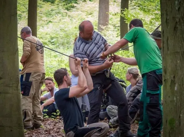 Teilnehmer üben eine Seilquerung mit einem Seil und Sicherheitsausrüstung im Wald