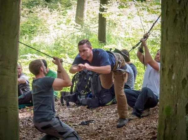 Teilnehmer überquert selbstgebaute Seilbrücke zwischen zwei Bäumen
