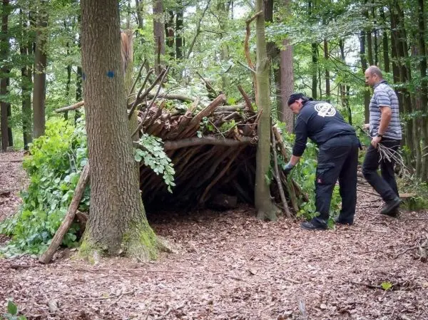 Zwei Personen bauen eine Laubhütte aus Ästen und Blättern im Wald
