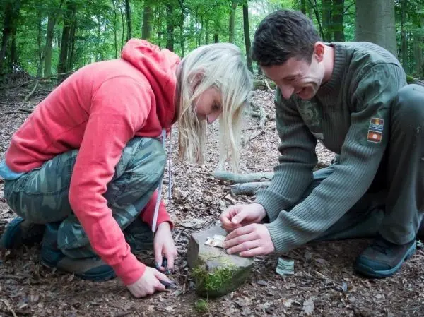 Zwei Personen bearbeiten einen Stein im Wald mit einem Messer
