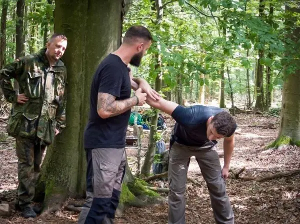 Zwei Personen demonstrieren eine Technik zur Armkontrolle an einem Baum im Wald