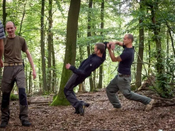 Zwei Personen führen eine Technik zur Kontrolle eines Gegners im Wald aus