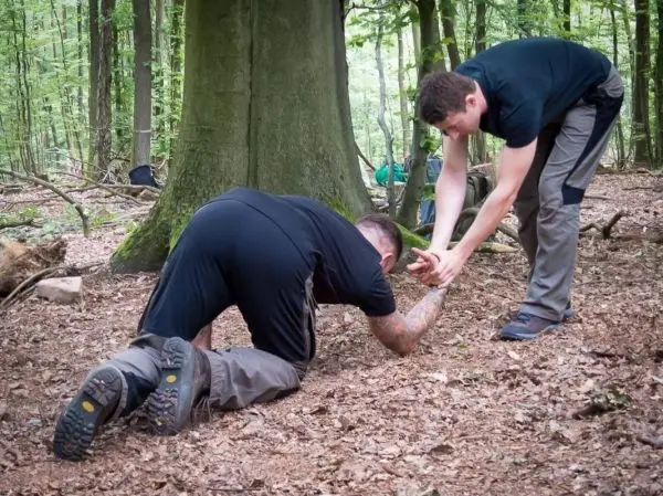 Zwei Personen helfen sich gegenseitig beim Krabbeln über den Waldboden