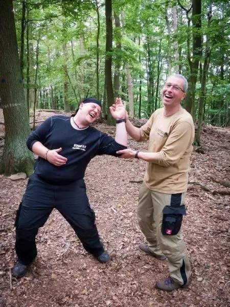Zwei Personen lachen und halten sich an den Händen im Wald