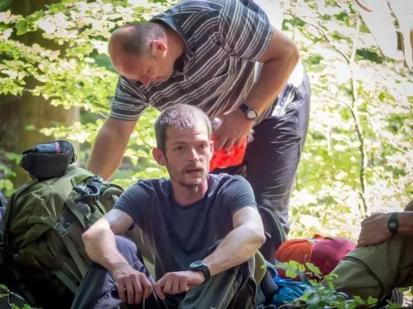 Zwei Personen sitzen in einem Wald neben Rucksäcken und Ausrüstung