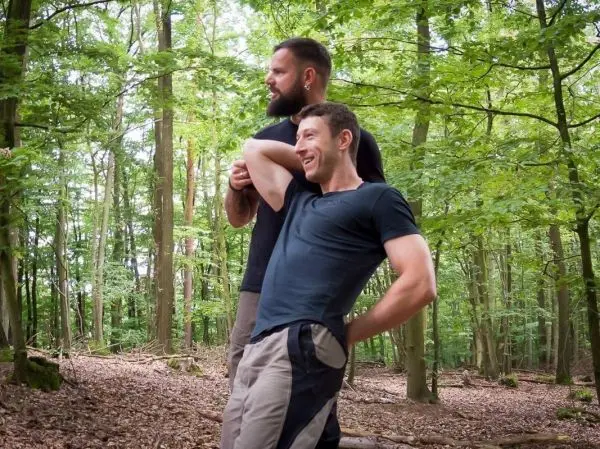 Zwei Personen stehen im Wald, eine Person lehnt sich nach hinten