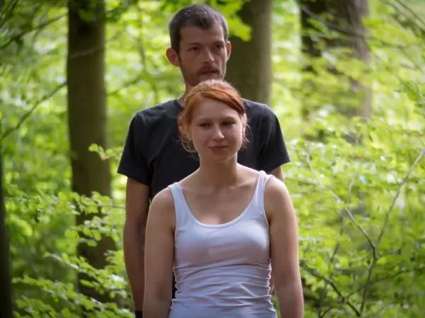 Zwei Personen stehen im Wald zwischen Bäumen und grünen Pflanzen