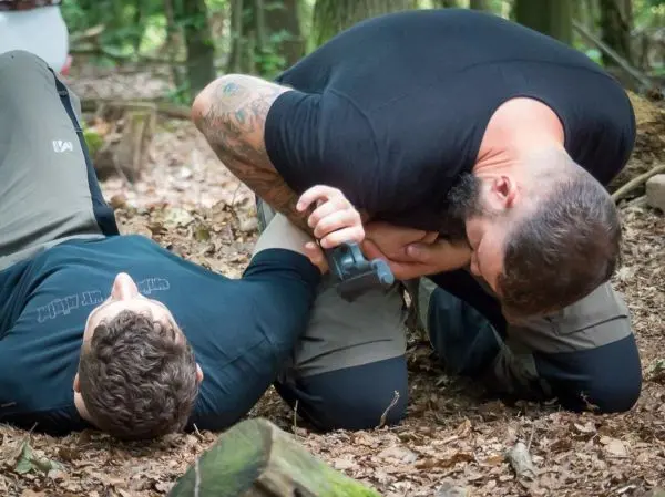 Zwei Personen üben eine Selbstverteidigungstechnik am Boden im Wald aus