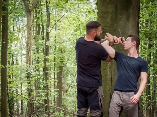 Zwei Personen üben eine Selbstverteidigungstechnik an einem Baum im Wald