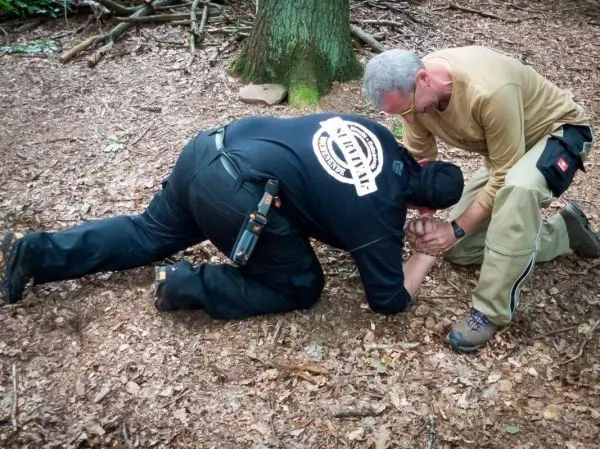 Zwei Personen üben eine Technik zur Handfesselung auf dem Boden im Wald