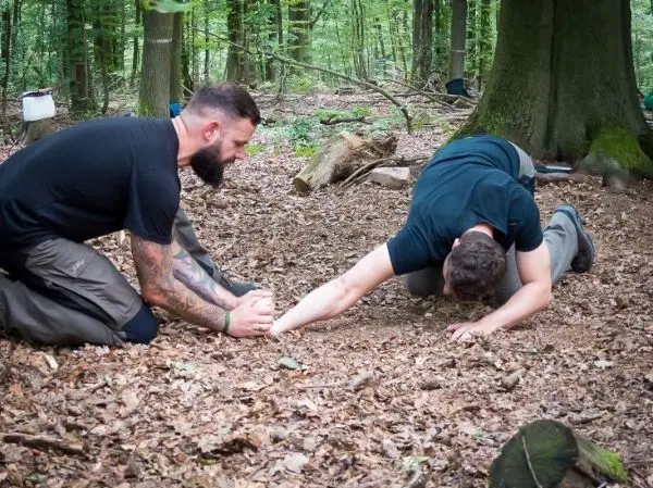 Zwei Personen üben eine Technik zur Unterstützung am Boden im Wald