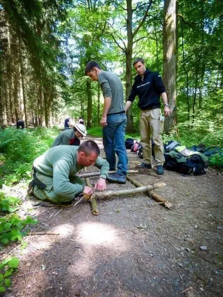 Drei Personen arbeiten an einer selbstgebauten Konstruktion aus Ästen im Wald