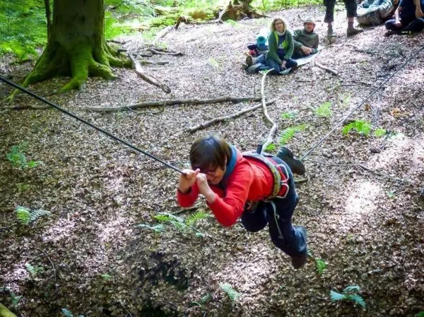 Junge überquert mit Sicherheitsgurt eine Seilquerung im Wald