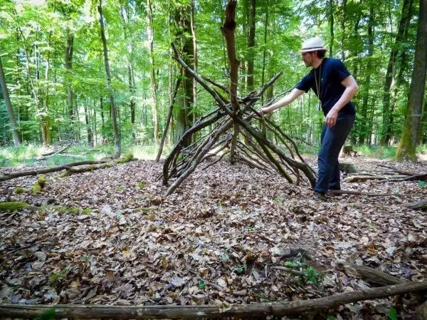 Mann konstruiert eine selbstgebaute Notunterkunft aus Ästen im Wald