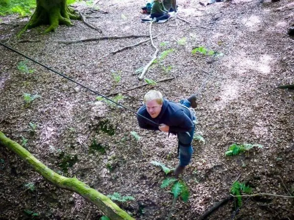 Mann überquert eine selbstgebaute Seilbrücke zwischen Bäumen