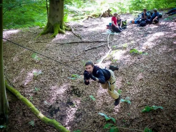 Mann überquert eine selbstgebaute Seilbrücke zwischen Bäumen