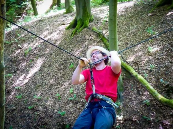 Mann überquert eine selbstgebaute Seilbrücke zwischen Bäumen