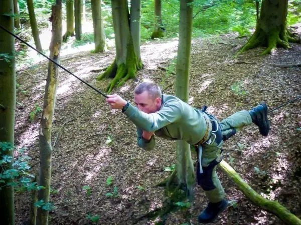 Mann überquert mit Seil eine Baumreihe im Wald
