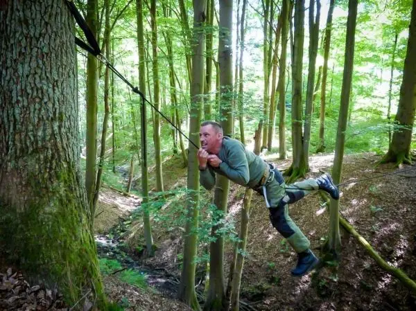 Mann überquert mit selbstgebauter Seilquerung einen kleinen Graben im Wald