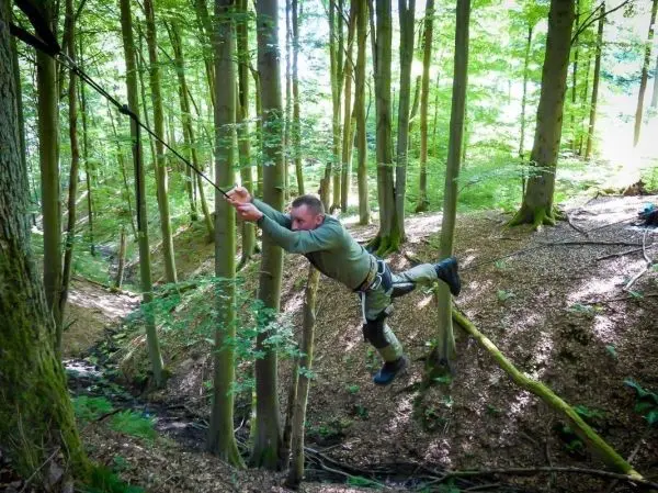 Mann überquert selbstgebaute Seilbrücke zwischen Bäumen im Wald