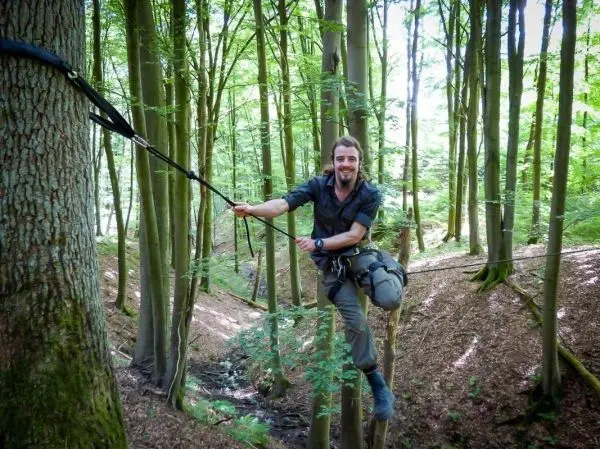 Mann überquert selbstgebaute Seilbrücke zwischen Bäumen im Wald
