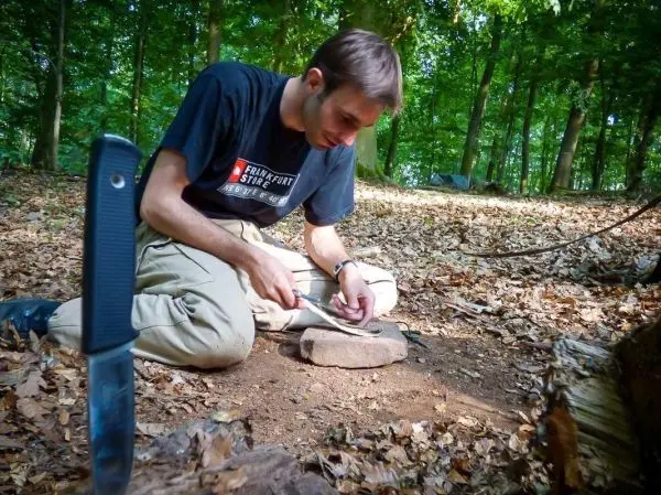 Messer schneidet Holzstück auf einem Stein im Laubwald