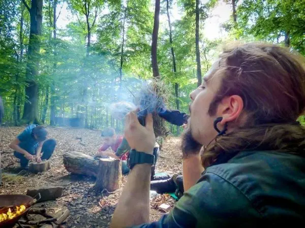 Person bläst in ein Bündel aus trockenem Material beim Feuer machen im Outdoorkurs