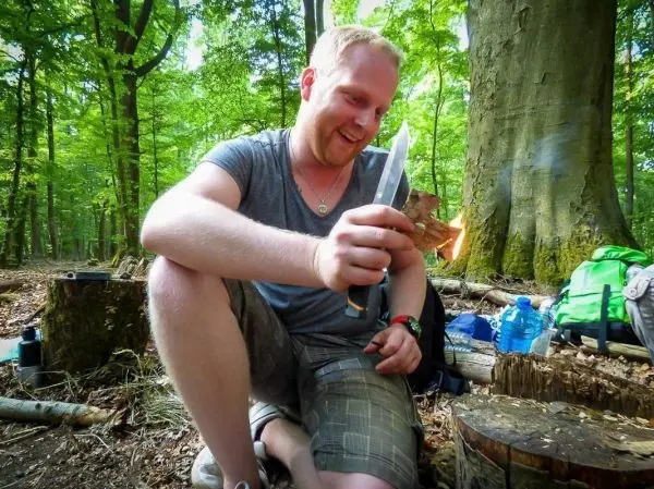 Person hält ein Messer und entzündet ein Feuerstück im Wald
