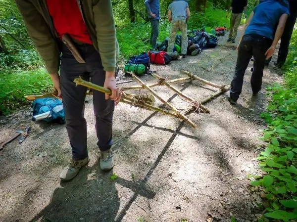 Person trägt eine selbstgebaute Trage durch den Wald beim Überlebenstraining