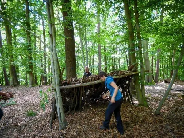 Person trägt einen Ast zu einer selbstgebauten Unterkunft im Wald