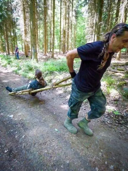 Person zieht eine andere Person auf einer selbstgebauten Trage durch den Wald beim Überlebenstraining