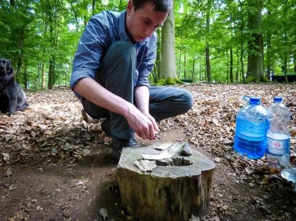Person zündet Feuerstelle auf Baumstumpf an beim Survival Training