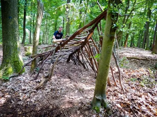Selbstgebaute Laubhütte aus Ästen im Wald, Person arbeitet daran