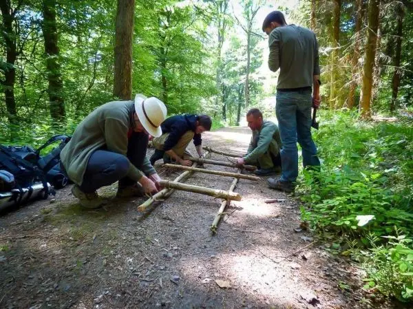 Vier Personen bauen eine selbstgebaute Trage aus Ästen im Wald