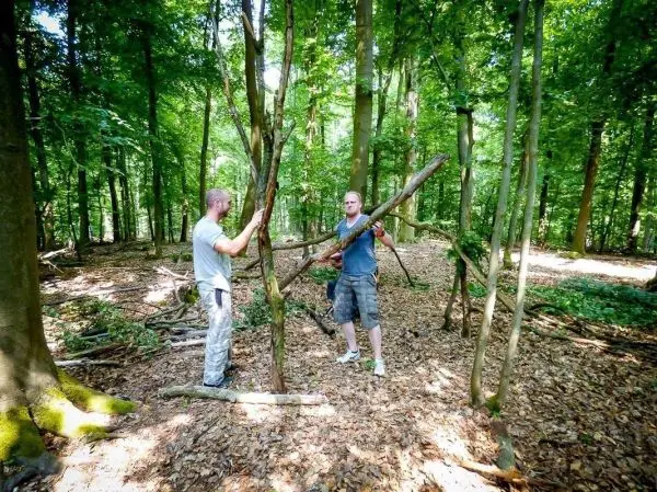 Zwei Personen bauen eine selbstgebaute Konstruktion aus Ästen im Wald