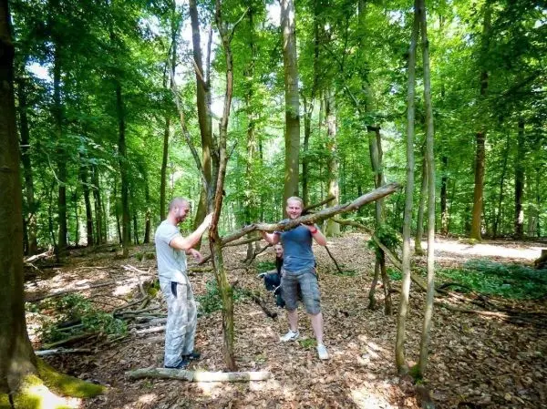 Zwei Personen bauen eine Struktur aus Ästen im Wald