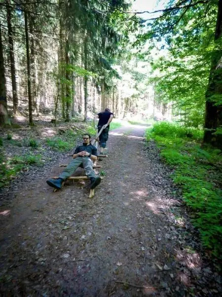 Zwei Personen nutzen eine selbstgebaute Trage auf einem Waldweg