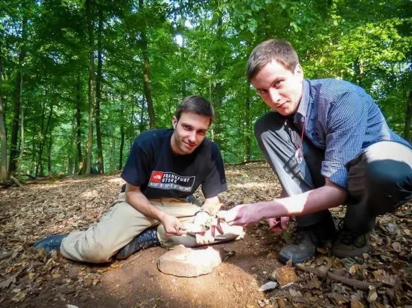 Zwei Personen zeigen eine Feuerstelle im Wald beim Überlebenstraining