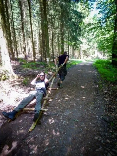 Zwei Personen ziehen eine improvisierte Trage aus Holz durch den Wald