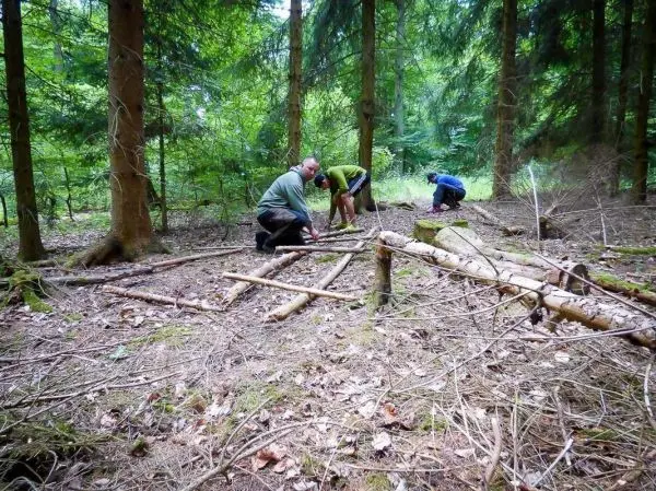 Drei Personen bauen eine Holzstruktur im Wald aus Ästen und Stämmen