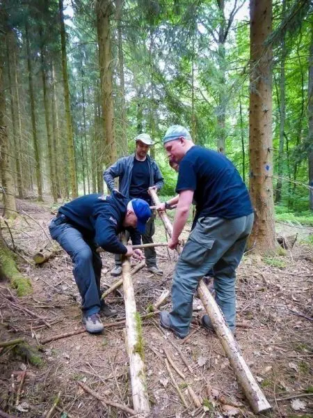 Drei Personen bauen eine selbstgebaute Konstruktion aus Holzstöcken im Wald